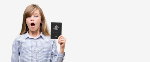 Young blonde toddler holding australian passport scared in shock with a surprise face, afraid and excited with fear expression