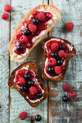 Quick breakfast, jam on toasts. Raspberry jam, ricotta and raw berries on ciabatta and rye bread on blue background