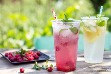 SOFT DRINKS. Refreshing summer drink lemon with mint, ice and raspberry with basil, ice. Glasses with cold and healthy beverage in a rustic style. Copy space.