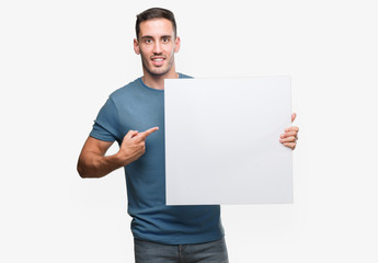Handsome young man holding advertising banner very happy pointing with hand and finger