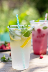 SOFT DRINKS. Refreshing summer drink lemon with mint, ice and raspberry with basil, ice. Glasses with cold and healthy beverage in a rustic style.