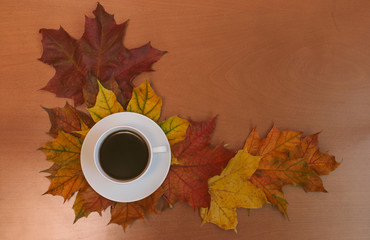 Cup of coffee with autumn maple leaves on wooden background