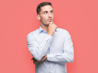 Handsome young businessman looking confident at the camera with smile with crossed arms and hand raised on chin. Thinking positive.