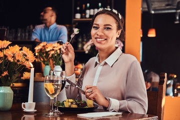 Portrait of a beautiful black-skinned woman wearing a blouse and flower headband, enjoying dinner while eating in a restaurant.