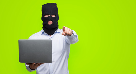 Business hacker man holding a computer laptop pointing with finger to the camera and to you, hand...