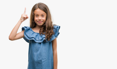 Brunette hispanic girl wearing denim dress surprised with an idea or question pointing finger with happy face, number one