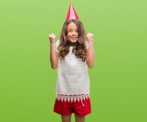 Brunette hispanic girl wearing birthday hat screaming proud and celebrating victory and success very excited, cheering emotion