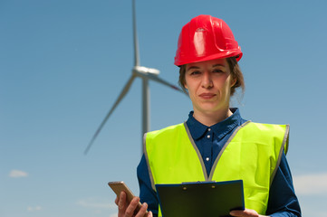 Portrait of a beautiful cute female engineer in a blue shirt in a red hard hat with an architectural plan in hand against the blue sky.