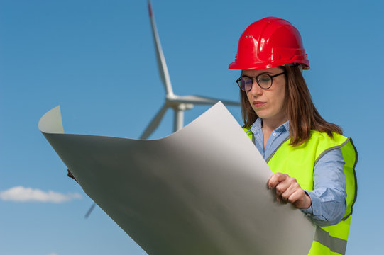 Serious young woman engineer looking at a plan of repair work on the background of a windmill