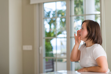 Down syndrome woman at home shouting and screaming loud to side with hand on mouth. Communication concept.