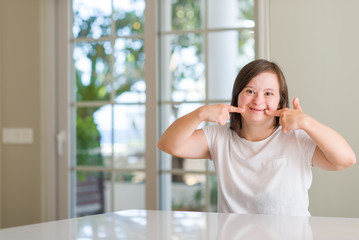 Down syndrome woman at home smiling confident showing and pointing with fingers teeth and mouth. Health concept.