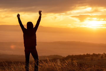 Man reaching summit enjoying freedom and looking towards mountains sunset.
