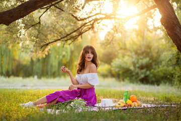 Obraz premium Beautiful girl with a peach in her hands on a picnic in the park. Looking away