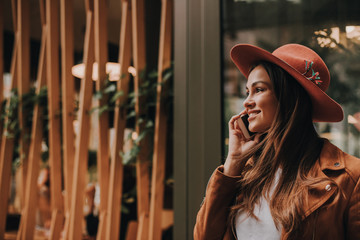 Horizontal picture of nice girl talking on the phone. She is posing. Girl is looking forward and smiling. She is standing inside of restaurant.