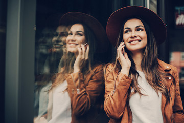 Attractive girl leaning to glass wall and talking on the phone. She looking at wall and smiling. Girl is posing. She is happy. Woman is smiling