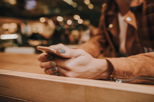 Cut view of woman's hands holding phone. She is sitting at table and using it