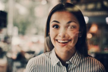 Portrait of girl stnading and looking on camera. She is smiling. Girl is standing behind glass wall. She looks happy