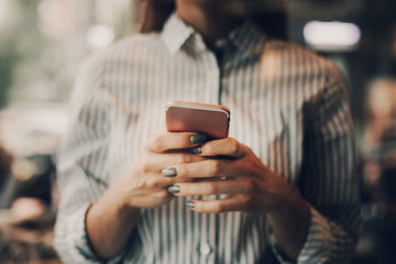 A pictute of girl in blouse standing and holding phone in hands. She is typing. Cut view