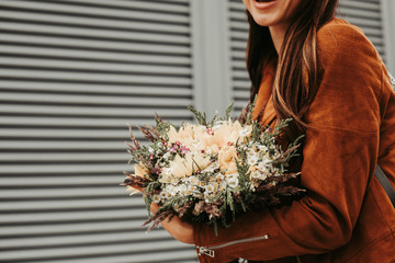 Cut view of girl holding flowers in hands. She is standing at wall. Girl wears brown jacket. Isolated on striped and white background