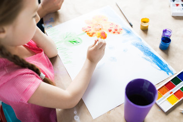 Little girl sitting at the table painting and using watercolor paints