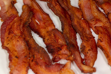 Slices of crispy bacon on a white plate for breakfast on the kitchen table waiting to be eaten