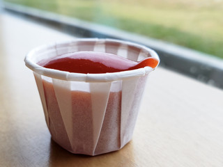 closeup of ketchup tomato sauce in a paper cup with blurred background under natural light