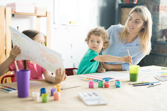 Little girl showing her picture to her mother and brother during painting at the table