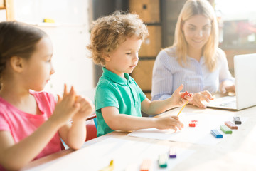 Little boy together with girl and teacher play dough and mold from plasticine