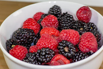 A white bowl with a mixture of raspberries and blackberries on a kitchen table waiting to be eaten 