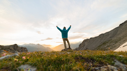 Fototapeta na wymiar Man standing on mountain top outstretching arms, sunrise light colorful sky scenis landscape, conquering success leader concept.