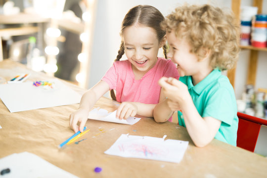 Two kids having fun at the table while drawing. They are writing letter on paper