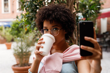 Female blogger taking a selfie on smartphone while drincking a coffee