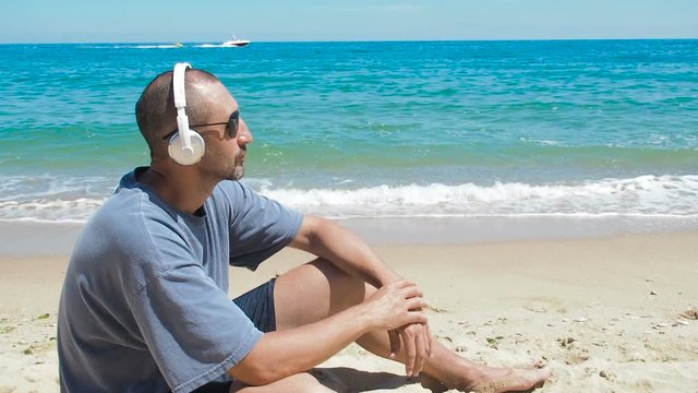 A man on vacation listening to music. A man on the beach listening to music on headphones.