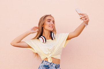 Portrait of beauty fashion smiling young women with wireless headphones making selfie. Flying hairs.