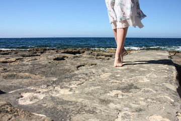 Legs of young girl in white fluttering skirt stand tiptoe on stone beach