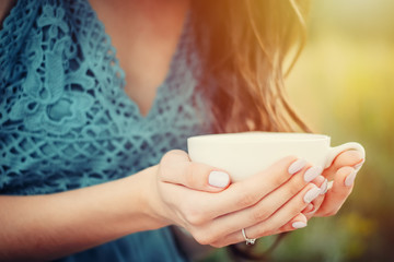 young woman or girl holds white cup in hands. Toned photo with summer sunlights