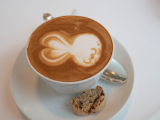 Cute latte art of sleep rabbit over freshly brew espresso coffee in a white porcelain ceramic cup with saucer and almond biscotti biscuit. Good for caffeine boost in the morning. Selective focus.