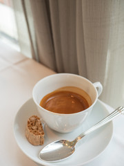 A shot of freshly brew espresso coffee with crema in a white porcelain ceramic cup with saucer and almond biscotti biscuit. Good for caffeine boost in the morning. Selective focus. Close up.