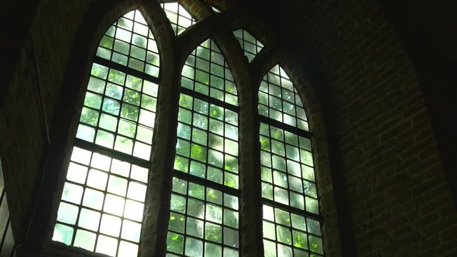 Indoor view of glass Church window on a sunny day with green trees swaying in the background