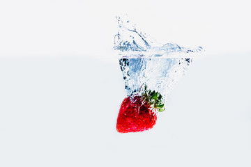 A fresh and delicious red strawberry isolated on a white background. Red strawberry dropping in water and creating a splash. The concept of healthy eating, consuming fruit.