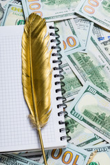 Notebook and Gold quill pen on dollar money background from one hundred dollars