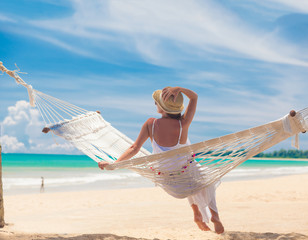 Young woman in white dress relaxing in a hammock by the beach
