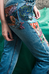 closeup of young woman in boho style blue jeans with colorful applications lower body