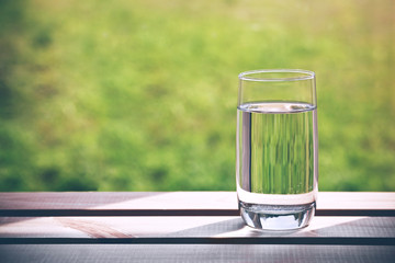 Glass of pure water on green natural background. Space for text