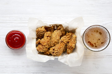 Chicken wings with ketchup, cold beer on a white wooden table, from above. Flat lay, overhead. Closeup.
