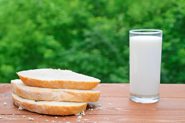 Sliced slices of wheat bread and a glass of milk. On a wooden table in the street in the summer.