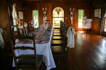 Intimate Wedding Reception Table Setting with White Table Cloth in a Wood Panel Restaurant Room with Stained Glass Window and Chandelier