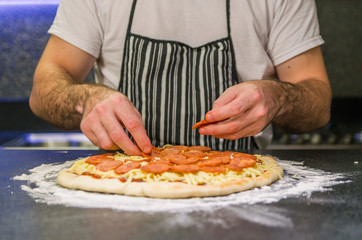 Obraz na płótnie Canvas Man preparing pepperoni pizza on black granite table