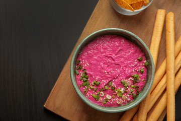 Flat lay composition with bowl of tasty beet hummus and bread sticks on dark background