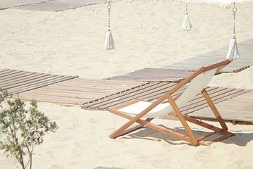 Espreguiçadeira em madeira na areia da praia numa zona com decoração tropical, vazia na praia,...